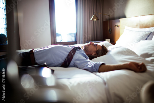Middle aged businessman lying down and resting on a bed in a hotel room after a long day of traveling and working photo