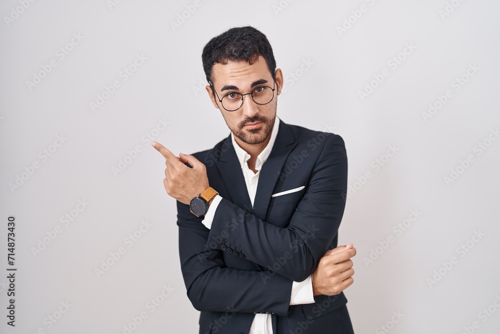 Handsome business hispanic man standing over white background pointing with hand finger to the side showing advertisement, serious and calm face Handsome business hispanic man standing over white background pointing with hand finger to the side showing advertisement, serious and calm face