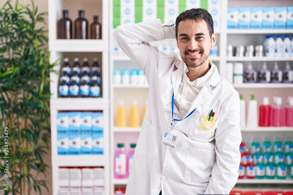 Handsome hispanic man working at pharmacy drugstore smiling confident touching hair with hand up gesture, posing attractive and fashionable