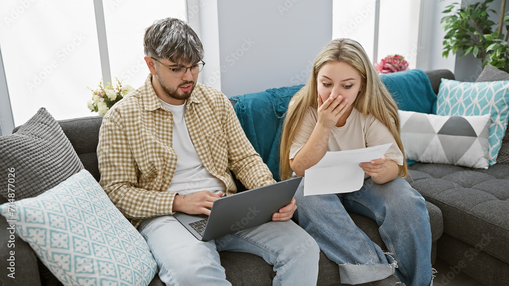 A distressed man and woman review documents on a couch, suggesting financial worries within a modern living room.