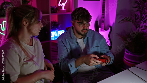 Couple enjoys gaming in a neon-lit home room at night, with a focused man and engaged woman.