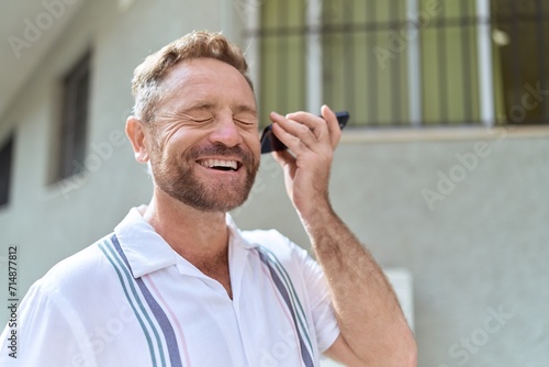 Middle age man smiling confident listening audio message by the smartphone at street