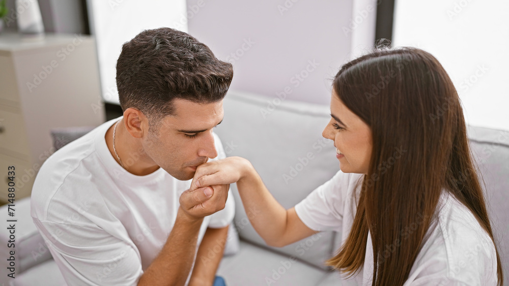 Fototapeta premium A loving couple in an intimate moment, man kissing woman's hand in a cozy living room setting.