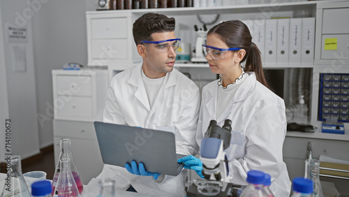 Man and woman scientists in lab coats discussing research using a tablet in a laboratory setting