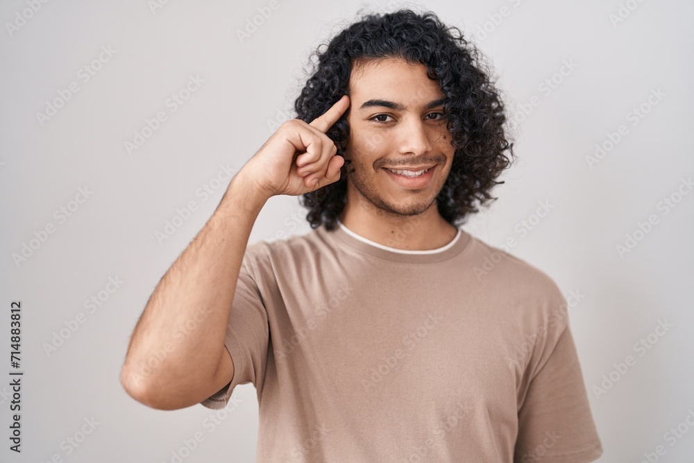 Hispanic man with curly hair standing over white background smiling pointing to head with one finger, great idea or thought, good memory Hispanic man with curly hair standing over white background smiling pointing to head with one finger, great idea or thought, good memory