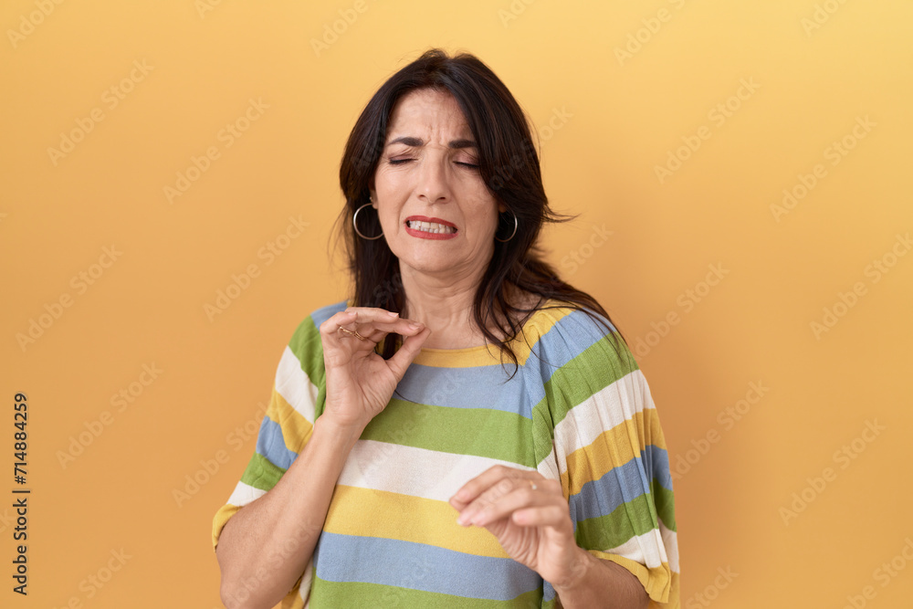 Middle age hispanic woman standing over yellow background disgusted expression, displeased and fearful doing disgust face because aversion reaction. with hands raised Middle age hispanic woman standing over yellow background disgusted expression, displeased and fearful doing disgust face because aversion reaction. with hands raised