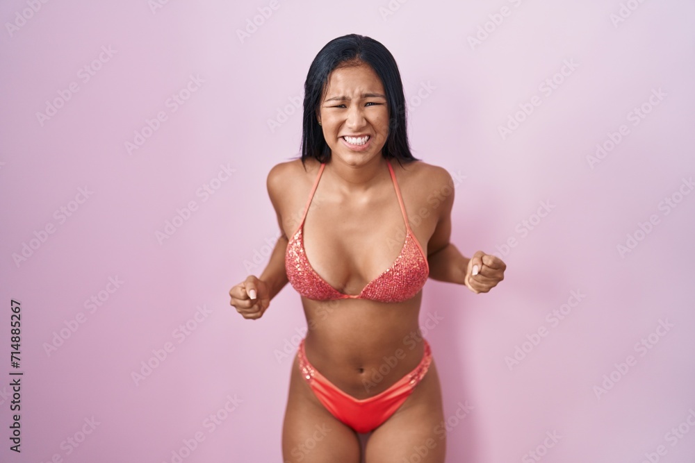 Naklejka premium Hispanic woman wearing bikini angry and mad screaming frustrated and furious, shouting with anger. rage and aggressive concept.