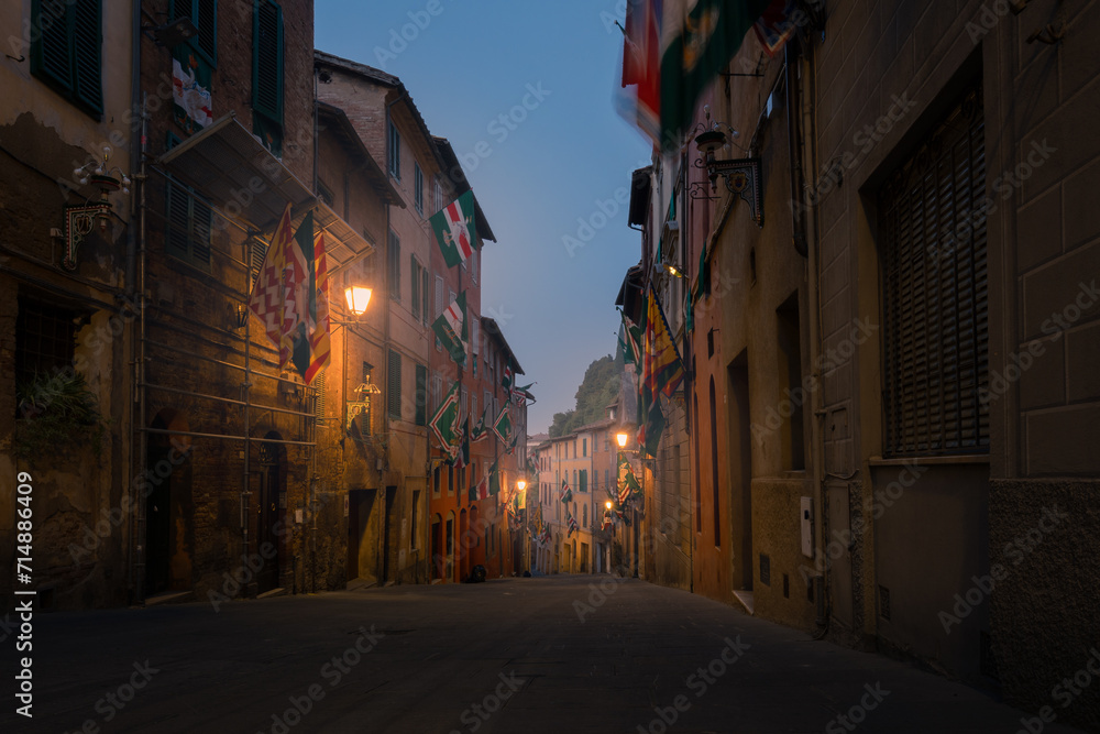 Dark narrow empty medieval street in the historical center of at night with rare lights, Siena, Italy