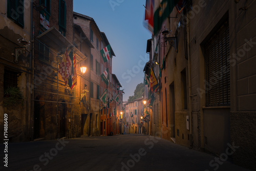 Dark narrow empty medieval street in the historical center of at night with rare lights, Siena, Italy