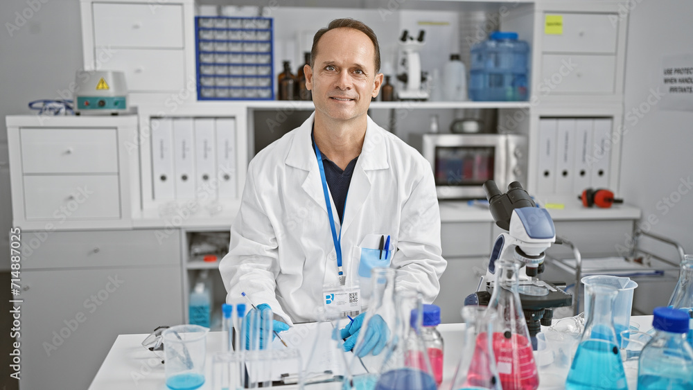 Handsome middle age man scientist, smiling confidently while jotting down notes for his research report in the bustling heart of a hospital laboratory. Handsome middle age man scientist, smiling confidently while jotting down notes for his research report in the bustling heart of a hospital laboratory.