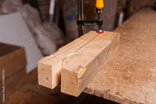 A carpenter works in a furniture workshop with various tools and a board