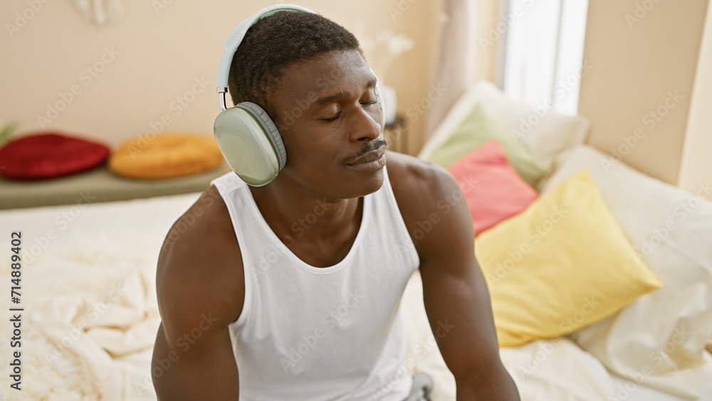 A relaxed african man chilling indoors on a bed, enjoying music with wireless headphones in a cozy bedroom. A relaxed african man chilling indoors on a bed, enjoying music with wireless headphones in a cozy bedroom.
