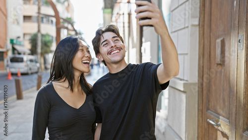 Interracial couple takes a selfie on a sunny city street, exuding happiness and love in an urban setting.
