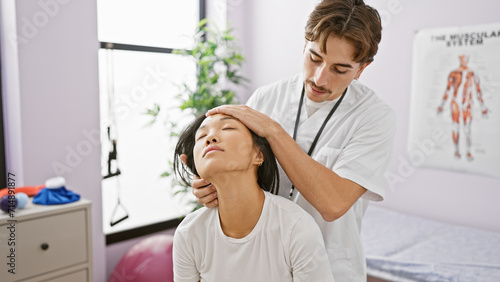 A male physiotherapist gently examines the neck of a female patient in an indoor rehabilitation clinic  with an anatomical poster in the background.