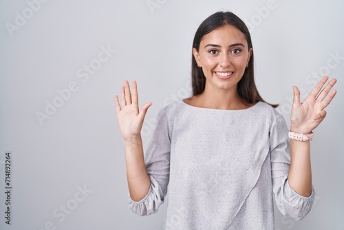 Young hispanic woman standing over white background showing and pointing up with fingers number nine while smiling confident and happy.