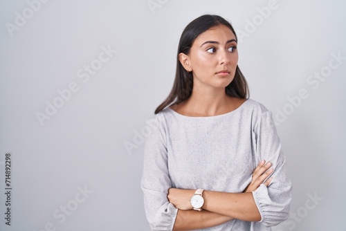 Young hispanic woman standing over white background looking to the side with arms crossed convinced and confident photo