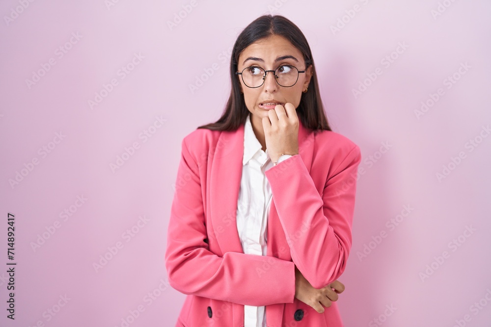 Young hispanic woman wearing business clothes and glasses looking stressed and nervous with hands on mouth biting nails. anxiety problem. Young hispanic woman wearing business clothes and glasses looking stressed and nervous with hands on mouth biting nails. anxiety problem.