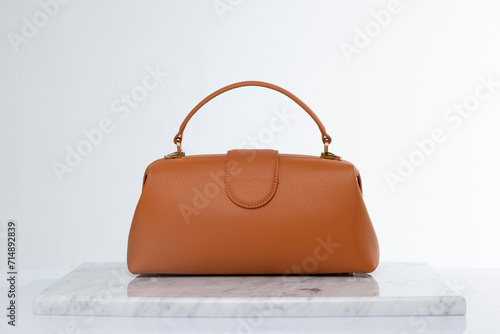 Luxury women's bag made of leather in brown and orange color tones, on a marble floor and white background in the studio