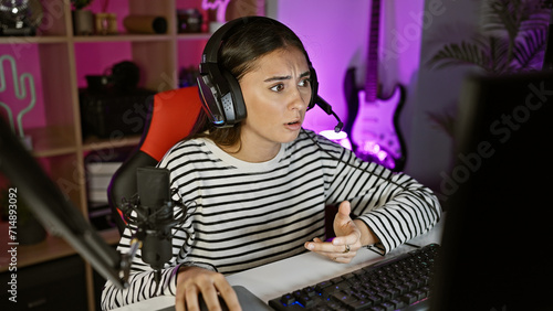 Hispanic woman reacts while gaming in a dark  colorful room with microphone and headset