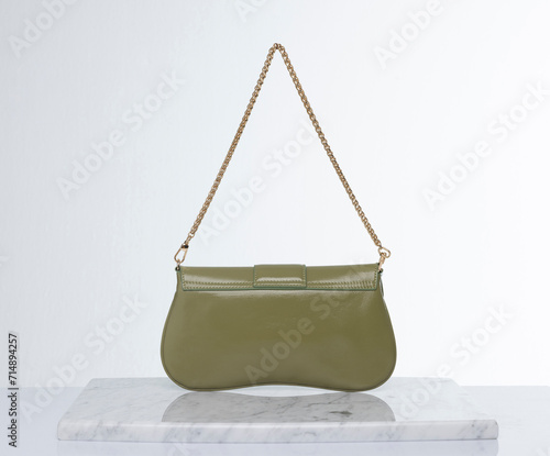 Green color, shiny leather bag with gold chain, on a marble floor and white background in the studio © Cumhur