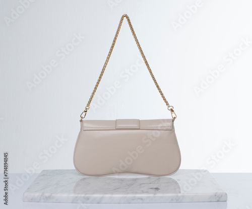 Light beige, shiny leather bag with gold chain, on a marble floor and white background in the studio © Cumhur