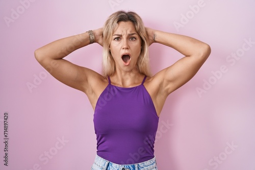 Young blonde woman standing over pink background crazy and scared with hands on head, afraid and surprised of shock with open mouth © Krakenimages.com