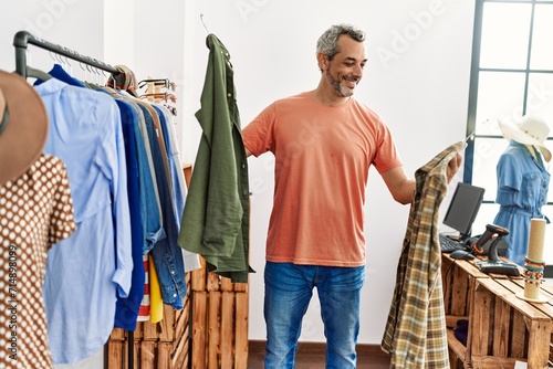 Middle age grey-haired man customer smiling confident holding clothes of rack at clothing store