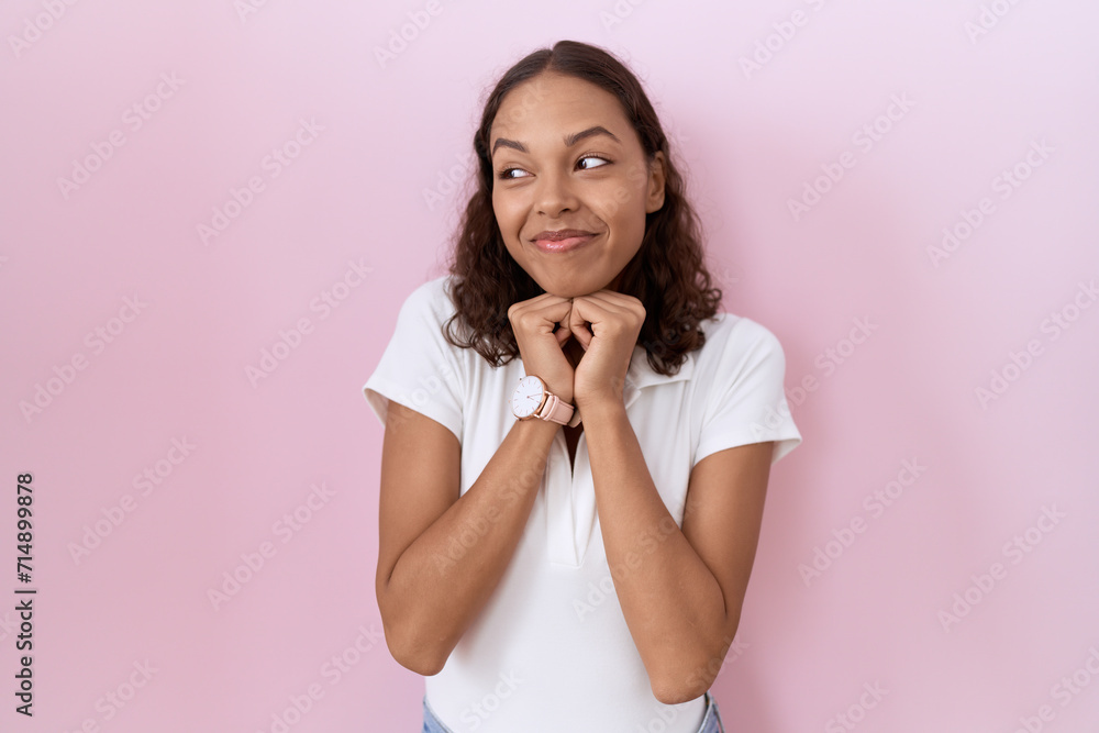 Young hispanic woman wearing casual white t shirt laughing nervous and excited with hands on chin looking to the side Young hispanic woman wearing casual white t shirt laughing nervous and excited with hands on chin looking to the side