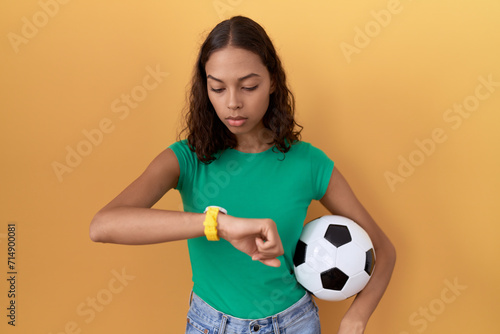 Young hispanic woman holding ball checking the time on wrist watch, relaxed and confident © Krakenimages.com