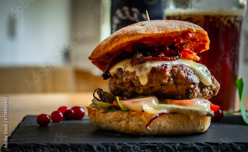 Homemade bacon cheeseburger on a dark tile with berries on the side and cold beer in the background. Food porn and nasty burger, smash burger