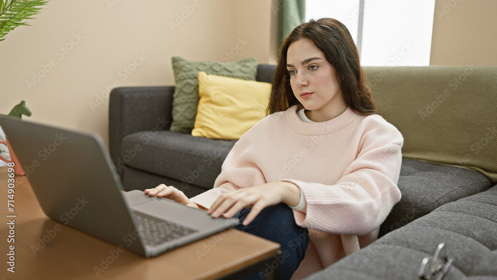 A contemplative young woman using a laptop in a cozy living room captures modern work-from-home lifestyle. A contemplative young woman using a laptop in a cozy living room captures modern work-from-home lifestyle.
