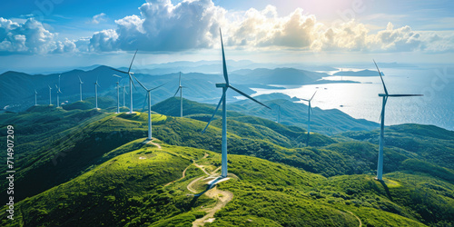 Wind turbines stand atop lush green hills with a panoramic view of the coast and sea, symbolizing sustainable energy generation. photo
