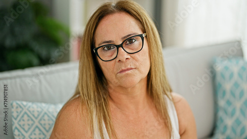 Middle age hispanic woman sitting on sofa with serious face at home