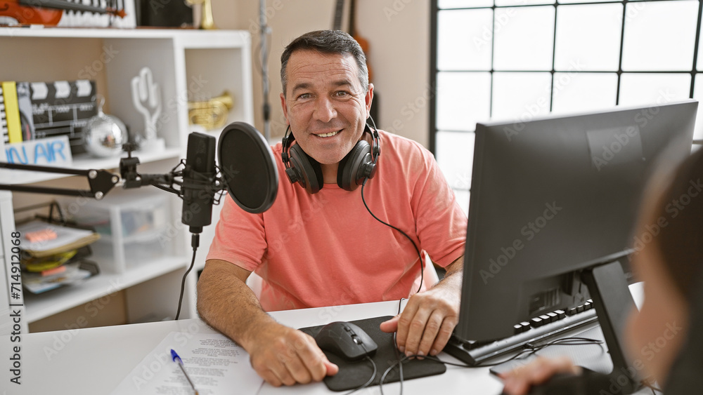 Smiling confident man and woman radio interviewers engaged in live broadcast in a professional radio studio, staged for speaking, listening, and delivering news on air Smiling confident man and woman radio interviewers engaged in live broadcast in a professional radio studio, staged for speaking, listening, and delivering news on air