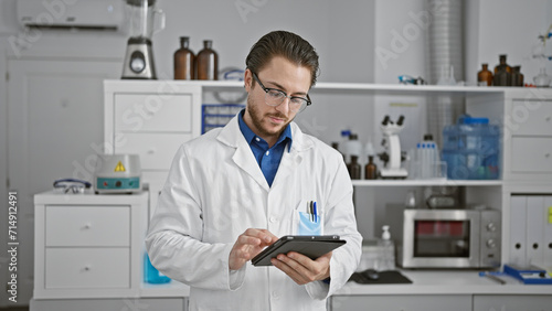 Young hispanic man scientist using touchpad at laboratory