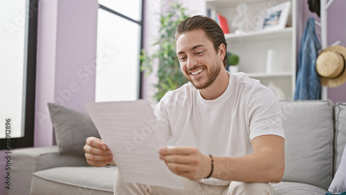 Young hispanic man reading document sitting on sofa smiling at home
