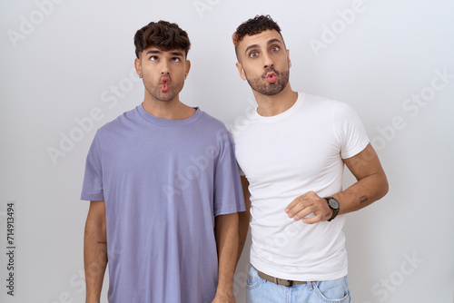 Homosexual gay couple standing over white background making fish face with lips, crazy and comical gesture. funny expression.
