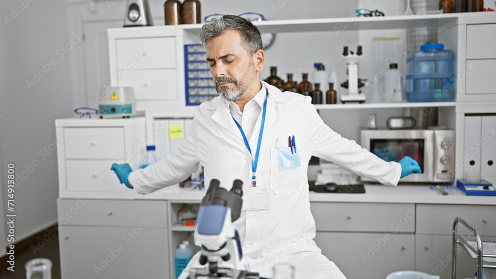 Handsome young hispanic grey-haired man, a diligent scientist stretching tired arms after long hours of intense medical research in the lab Handsome young hispanic grey-haired man, a diligent scientist stretching tired arms after long hours of intense medical research in the lab