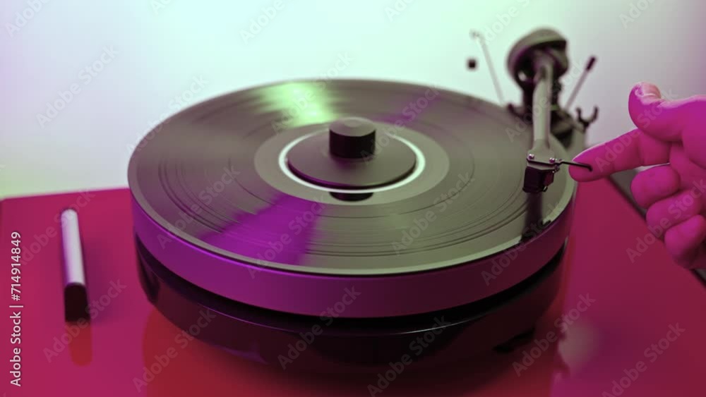 View of a person's hand operating a vinyl record player to listen to music. View of a person's hand operating a vinyl record player to listen to music.