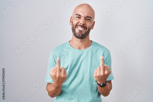 Middle age bald man standing over white background showing middle finger doing fuck you bad expression, provocation and rude attitude. screaming excited photo