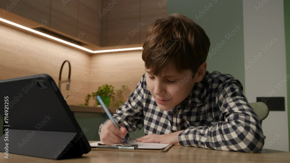 Kid with Autism writes with focus while using a tablet computer. Illustrates the unique blend of creativity and technology in neurodiverse learning. Kid with Autism writes with focus while using a tablet computer. Illustrates the unique blend of creativity and technology in neurodiverse learning.