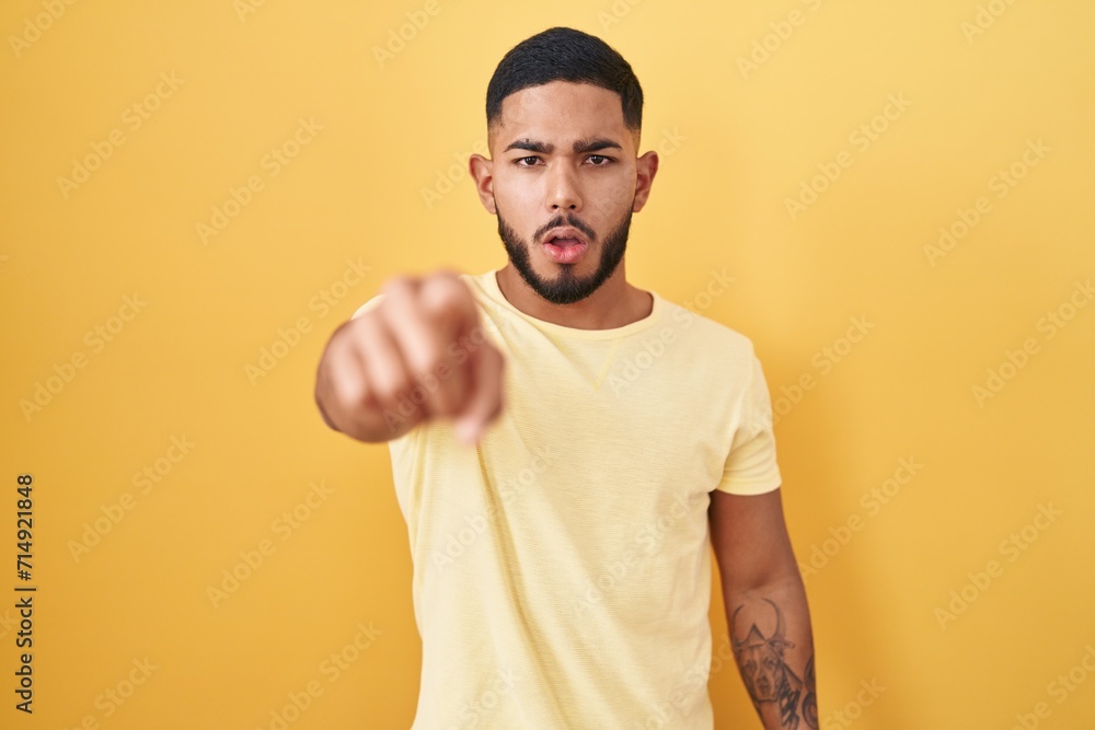 Young hispanic man standing over yellow background pointing displeased and frustrated to the camera, angry and furious with you Young hispanic man standing over yellow background pointing displeased and frustrated to the camera, angry and furious with you