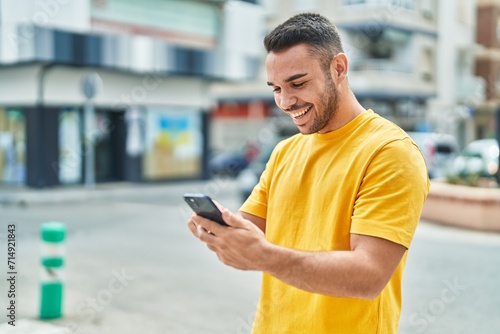 Young hispanic man smiling confident using smartphone at street photo