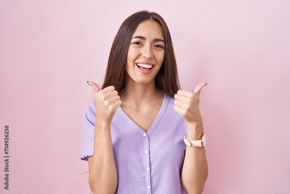 Young hispanic woman with long hair standing over pink background success sign doing positive gesture with hand, thumbs up smiling and happy. cheerful expression and winner gesture. Young hispanic woman with long hair standing over pink background success sign doing positive gesture with hand, thumbs up smiling and happy. cheerful expression and winner gesture.