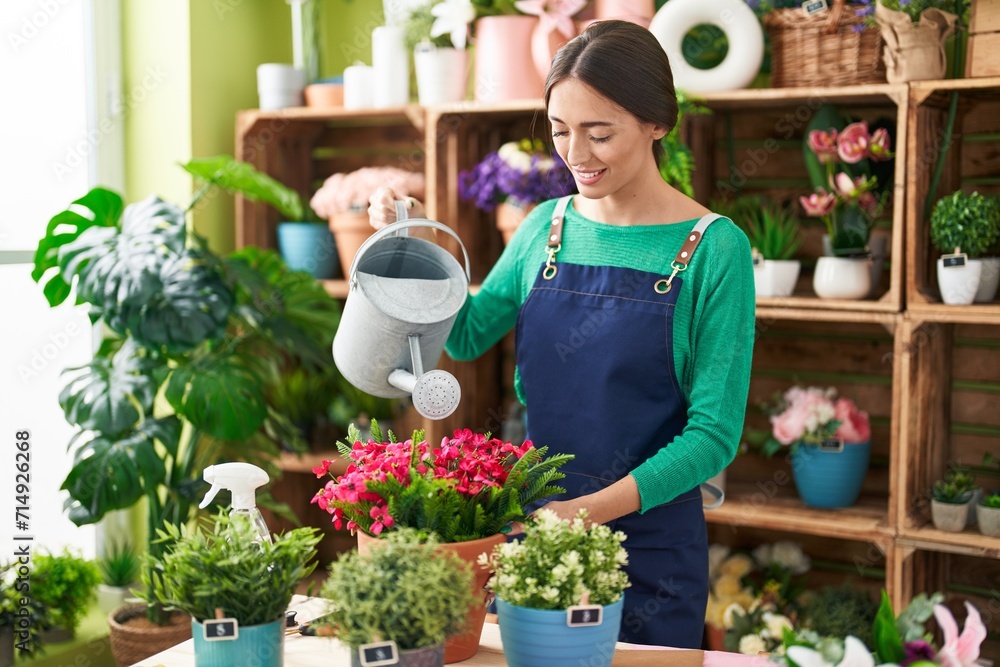 Young beautiful hispanic woman florist smiling confident watering plant at flower shop