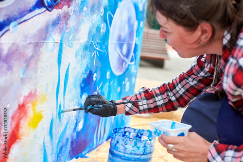 Female painter draws picture with paintbrush on canvas for outdoor street exhibition, close up side view of female artist apply brushstrokes to canvas, symphony of art creativity photo