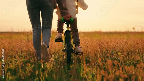 Childhood dream to ride bike. Family game, mom kid, to pedal. Mother teaches her little daughter to ride bike on grass in park. Young mom teaches her child to maintain balance while sitting on bicycle photo