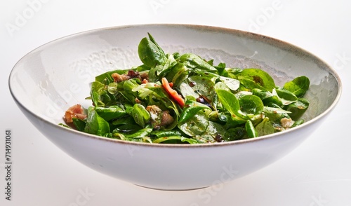 Fresh spinach salad with bacon, walnuts, and vinaigrette in a white bowl on a clean background.