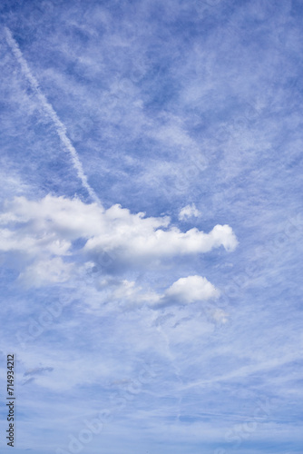 A serene sky with scattered fluffy clouds, contrails, wispy cirrus, and a backdrop of tranquil blue.