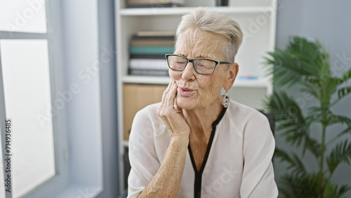 Senior grey-haired woman business worker in office, aching toothache pains strike during workday photo